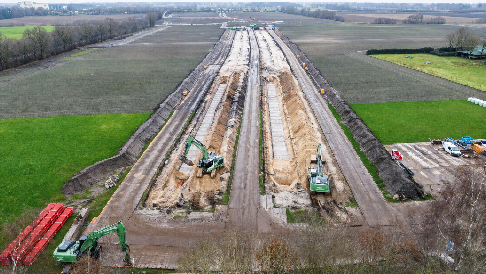 Luftaufnahme einer Baustelle mit Baggern und langen Ausgrabungsgräben inmitten von Feldern